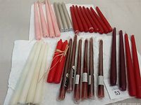Photo showing 40 tapered candles of various colors and lengths spread on white surface including white, pink, silver, red, brown, burgundy