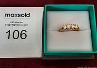 Image of gold tone ring with four clear stones in green jewelry box with inventory number.