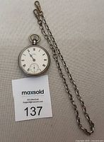 Full view of antique Waltham silver pocket watch with attached chain laid out flat on fabric background