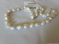 White baroque pearl necklace laid out loosely on a light surface showing individual pearls and gold clasp.