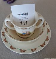 Stacked view of two-handled cup inside bowl inside plate showing Bunnykins designs and condition