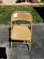Front view of one tan heavy duty folding chair showing plastic seat and backrest with metal frame.