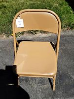 Front view of one tan heavy duty metal folding chair, showing the padded seat and backrest.