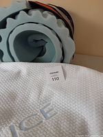 Photo showing the rolled-up light blue convoluted foam mattress topper and white woven cooling cover with 'ICE' branding.