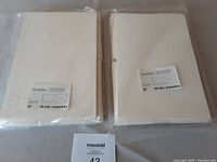 Two unopened packs each containing 50 sets of Revolution cream coloured A7 cardstock cards and envelopes.