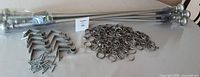 Set of adjustable silver metal curtain rods with round decorative end caps laid out alongside several metal mounting brackets, curtain rings with hooks, and screws.