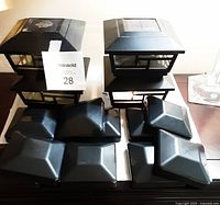Four black solar light deck post caps with window panes for LED illumination and ten black plain caps shown on table.