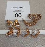 Four pairs of gold-tone and rhinestone earrings displayed on a neutral fabric background with lot number card.
