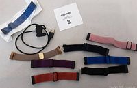 Photo of seven Fitbit Charge 5 wristbands in various colors and one USB charger cable.