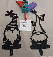 Photo showing two black metal gnome garden decorations and one colorful wooden bird outdoor decoration.