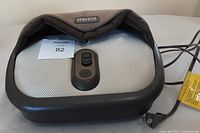 Front view of the Homedics foot warmer and massager device showing brand logo on upper front and control panel with power cord on the side.