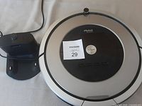 iRobot Roomba 800 round robot vacuum with charging dock on surface, showing top with Clean button and brand labeling.