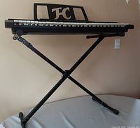 Full electronic keyboard on adjustable black X-style metal stand against wall.