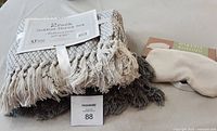Two cotton throw blankets in light gray and dark gray with fringed edges and a soft beige eye pillow.