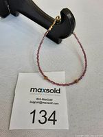 Full view of delicate pink Swarovski crystal bracelet hanging from black display stand showing gold-tone clasp and overall length.