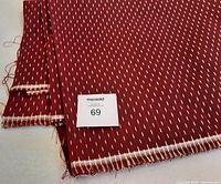 Folded piece of deep red fabric with gold thread details laid flat showing length and frayed edges.