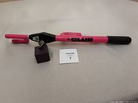 Pink and black The Club steering wheel lock lying flat showing the lock mechanism and included key, against a plain background.