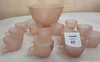 Set of 12 pink frosted glass cups arranged in front of large punch bowl with ladle; shows full set and scale