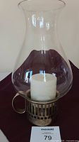Full view of vintage hurricane candle lamp with clear glass shade, brass base, and white candle inside.