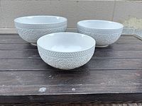 Three white stoneware bowls showing embossed harvest pattern outside and smooth glazed interior on wooden surface