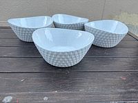 Four white textured diamond pattern porcelain bowls displayed together on a dark wooden surface.