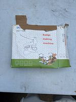 Box of a badge making machine model DC-109, showing packaging with machine illustration and text.