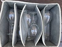 Five clear glass wine glasses packed upright in gray woven container with dividers.