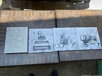 Four square pieces of wall decor laid out on wood table: three black and white Chanel art prints and one glitter-text plaque with motivational quote.