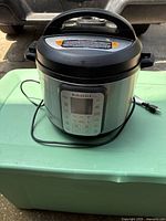 Front angled view of Instant Pot showing digital control panel and power cord wrapped around base on green plastic surface.