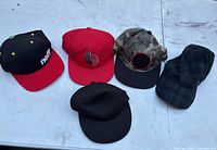 Photo showing five men's snapback hats in a row on a light surface, featuring various colors and logos.
