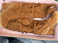Pair of women's tan suede boots with wrap-around straps displayed inside a box.