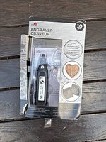Photo of new Plaid engraver machine in original box showing the tool and included engraving tips. Packaging indicates 10 pieces and different materials it works on.
