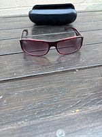 Front view of Ralph Lauren women's sunglasses in red frame with purple lenses on wooden surface with black case behind.