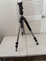 Full view of the Ravelli tripod showing three silver adjustable legs, black foam grip, and black mounting head