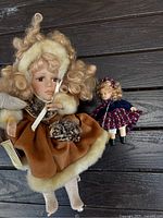 Front view showing large Tiffany Victorian doll in brown fur-trimmed coat and smaller doll in blue jacket and plaid dress.