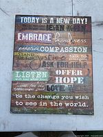 Rectangular wooden sign with distressed rustic finish and multi-colored horizontal stripes with white and black inspirational text phrases.