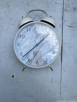 Front view of white round decorative stand-up clock with twin bells and black hour numerals