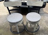 Two white wooden swivel barstools with round light gray fabric cushions and low backs shown from the front on pavement.