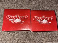 Two red Kwikset branded boxes labeled 'The Key to Security', containing the door handle sets.