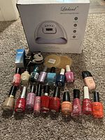 Photo showing all nail polishes laid out in front of the open box Liteland LED UV Nail Lamp along with two novelty soaps and two boxed beauty items