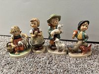 Four Goebel porcelain figurines of children with animals, shown side by side on carpeted floor.