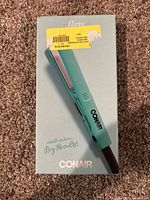 Front view of retail box showing turquoise Conair mini hair straightener with ceramic plates, model named 'flirty'.