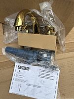 Delta polished brass bathroom faucet with two handles, partially packaged with plastic wrap and cardboard support, showing overall condition and components.