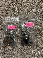 Two dragonfly pendants with metal wings and stones as bodies, in plastic bags