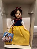 Full view of the Snow White doll inside original box. Doll wears classic blue, white, and yellow costume with red ribbon in hair. Doll holds collectible tag.