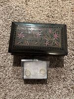 Overhead photo showing decorative floral trinket box and pair of small gold-tone diamond hoop earrings in protective plastic.