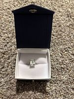 Top view of silver ring with green amethyst gemstone in blue jewelry box on carpet surface.