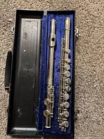 The flute disassembled inside the black hard-shell carrying case with blue lining, showing the headjoint and body sections securely positioned.