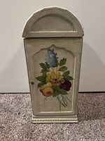 Front view of cream-colored wooden shelving unit with hand-painted floral door.