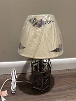 Full view of the metal table lamp with fabric lampshade showing pressed flowers covered in plastic wrap, lamp cord attached.